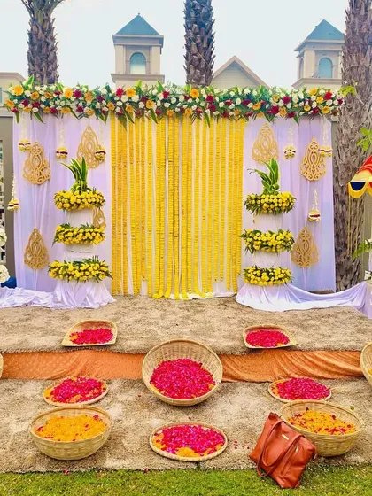 An elegant Haldi stage setup with a white and yellow theme. We used tiered floral stands, traditional umbrellas, and baskets filled with fresh marigold and rose petals.