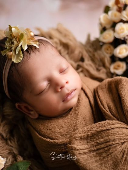 A close-up portrait showcasing an earthy, brown-toned wrap and a delicate floral headband. The focus here is on the baby's peaceful expression.