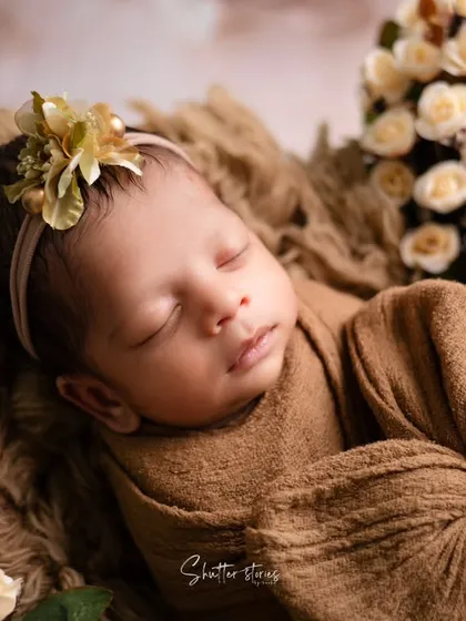 A close-up portrait showcasing an earthy, brown-toned wrap and a delicate floral headband. The focus here is on the baby's peaceful expression.
