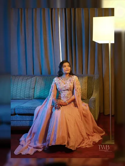 A modern and elegant portrait. The bride, in a flowing peach gown with cape sleeves, sits gracefully on a sofa, looking like a princess from a fairytale.