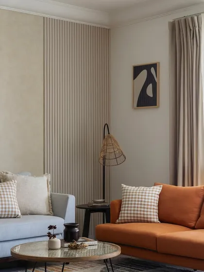 This living room celebrates minimalism with earthy tones and subtle textures. The combination of a powder blue and a burnt orange sofa adds warmth, while the fluted and lime-washed wall panels provide a tactile backdrop.