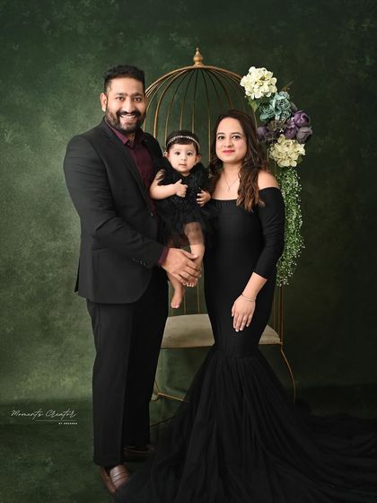 A formal family portrait with a touch of regal elegance. The golden birdcage prop adds a unique visual element to this beautifully composed shot against a deep green backdrop.