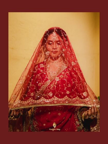 The bride holds her sheer red veil, her expression serene and thoughtful. This portrait captures the traditional beauty and quiet grace of the moment.