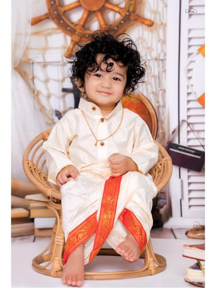 A handsome little boy dressed in a traditional veshti, sitting proudly in a wicker chair. This classic portrait is perfect for celebrating cultural milestones and family traditions.