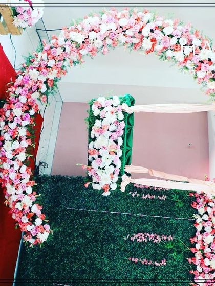 A lovely floral arch made of pink and white roses, set against a green wall for a cradle ceremony. This decoration creates a beautiful frame for the baby's cradle, symbolizing a blessed welcome.