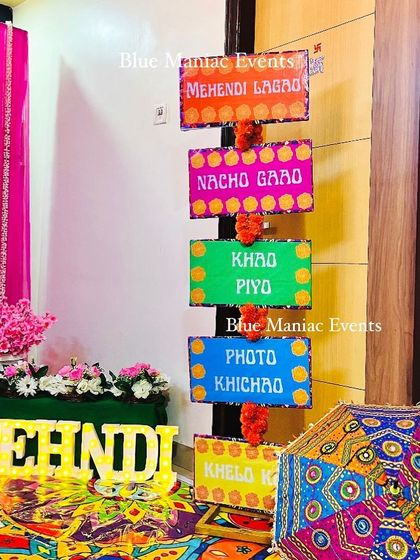 Fun and quirky props for a Mehendi party, including 'Mehendi Lagao' signs and marquee letters, set against a colorful backdrop.