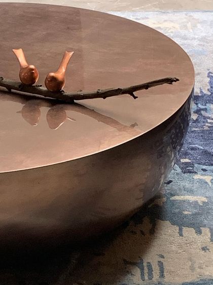 Even small objects can tell a story. This hammered copper coffee table holds a simple bronze sculpture of two birds on a branch, a detail that brings a touch of nature and artistry to the living space.