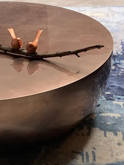 Even small objects can tell a story. This hammered copper coffee table holds a simple bronze sculpture of two birds on a branch, a detail that brings a touch of nature and artistry to the living space.