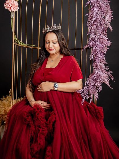 A regal maternity look with the mother-to-be in a stunning red gown and a crown. The makeup is glamorous and elegant, making her look like a queen.