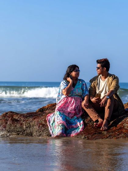 A candid conversation between a couple sitting on a rock by the sea. The waves crashing nearby add a dynamic element to this relaxed beach pre-wedding photograph.