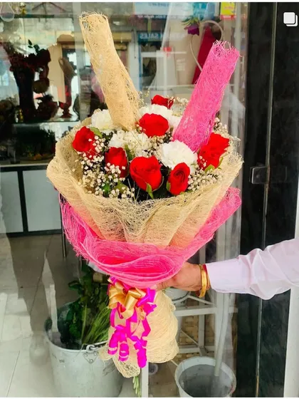 A creative bouquet using mixed materials for wrapping, including natural and pink jute netting. The flowers are a classic mix of red roses and white chrysanthemums.