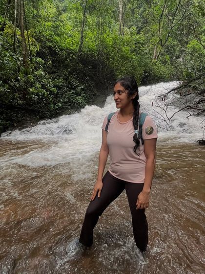 A smiling trekker stands in the flowing waters of a stream on the Kodachadri trail.