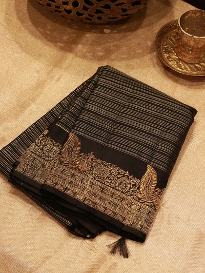 A traditional black Kanjivaram with exquisite peacock motifs and intricate gold lines, a timeless classic.