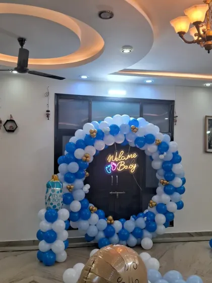 This is a classic "Welcome Boy" decoration featuring a full ring balloon arch in blue, white, and gold. The bright "Welcome Boy" neon sign makes it a perfect photo backdrop for your celebration at home.