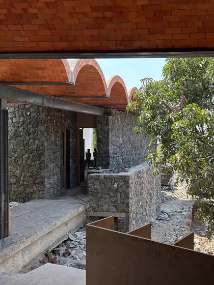 A view through a developing corridor at the Karjat residence, highlighting the material palette of local stone and brick jack arches. These natural materials root the modern structure in its specific place.
