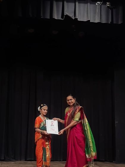 Presenting a certificate to a young student in her vibrant orange and green costume. These moments on stage are what we work towards in our classes, building confidence and performance skills.