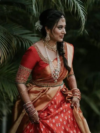 A bride in a red half-saree ensemble. Her custom red blouse features delicate gold embroidery, completing her traditional yet youthful look.
