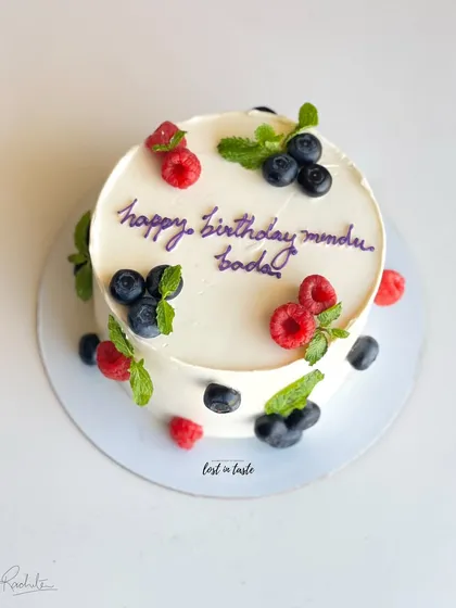 A simple yet beautiful celebration cake with chocolate buttercream, decorated with fresh raspberries, blueberries, and mint leaves for a pop of color and flavor.