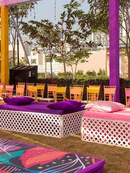 Comfortable and stylish low seating for guests at a Haldi. The vibrant purple and pink cushions complement the colorful overhead drapes, creating a cohesive and inviting lounge area.