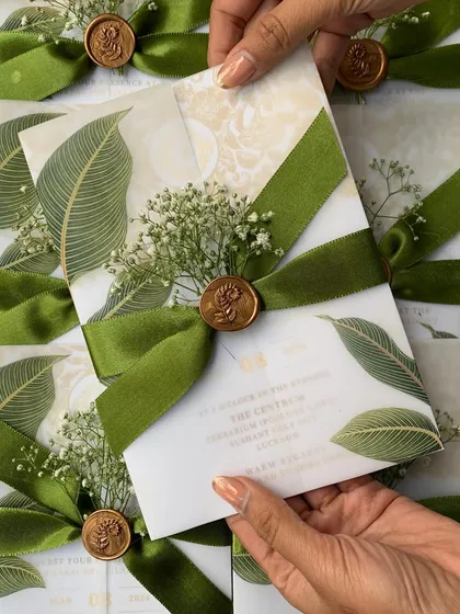 We believe in the beauty of minimalism. This engagement invitation features a vellum wrap with a banana leaf print, held together by a rich green velvet ribbon, a custom wax seal, and a sprig of fresh baby's breath for a touch of natural elegance.