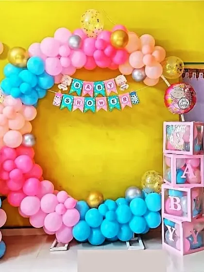 A bright and cheerful baby shower setup against a yellow wall. The multi-colored balloon ring and 'BABY' blocks make for a very happy and festive celebration.