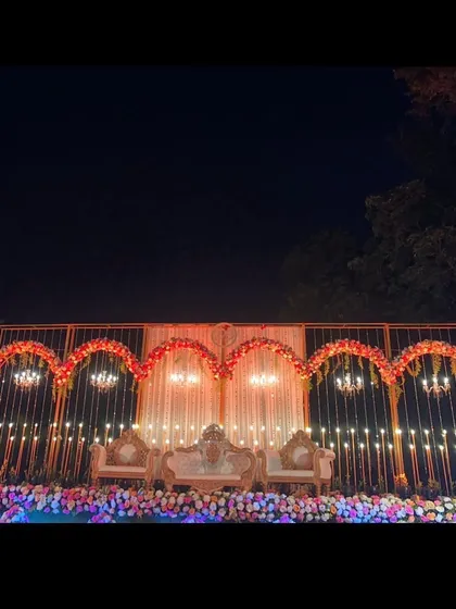 A stunning reception stage setup for a destination wedding in Lonavala. The design features a series of golden arches adorned with red and pink flowers, chandeliers, and beautiful hanging lights.