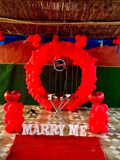 This is a popular proposal decoration package. It features a full circle balloon arch in vibrant red, "MARRY ME" marquee letters, and a small table for a cake or champagne, perfect for a terrace or garden proposal.