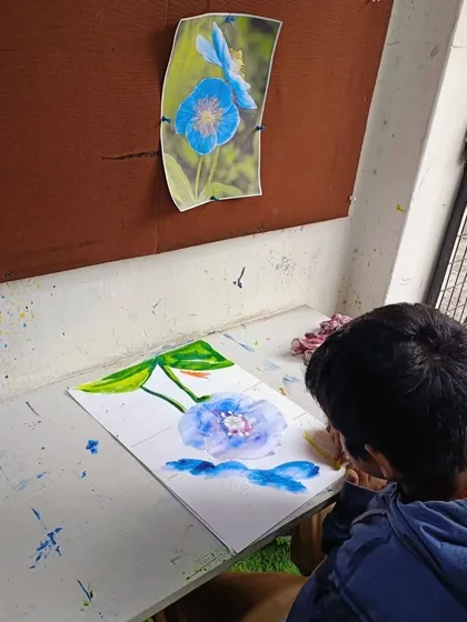 A student at work on his blue flower painting. He is using a reference photo to guide his watercolor application.
