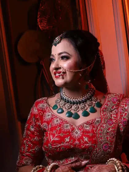 A bride in a red lehenga wearing a statement necklace with large green stones. This Polki set is designed to be the centerpiece of your bridal look.