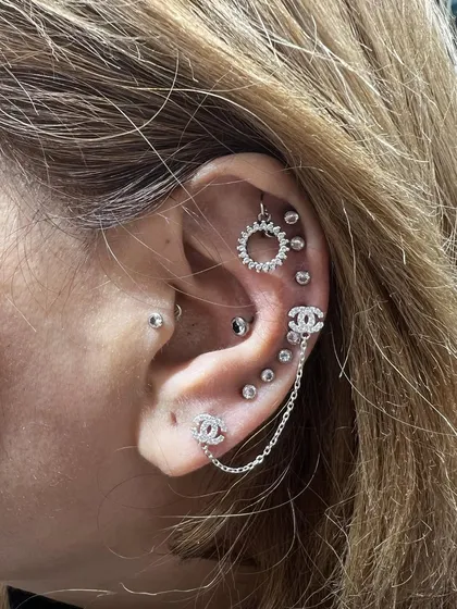 A luxurious ear stack featuring Chanel-inspired studs connected by a chain and a sunburst helix hanging.