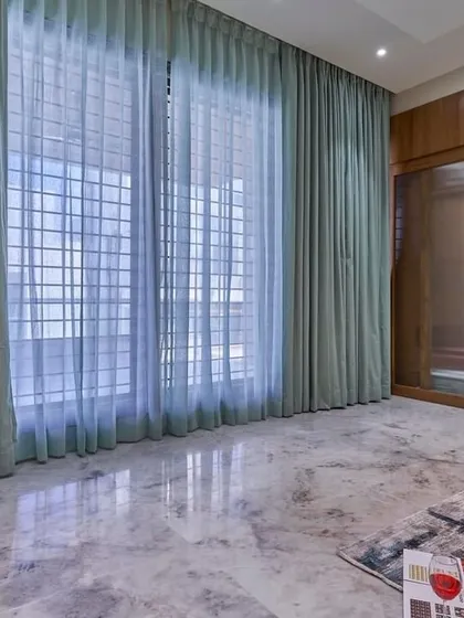 This image highlights the sheer and blackout curtains that provide versatile light control and privacy. The expansive marble floor reflects light, making the room feel bright and airy.