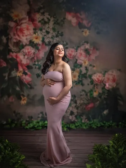 A simple yet elegant portrait. The mom-to-be wears a form-fitting gown that beautifully accentuates her silhouette against the soft floral background.