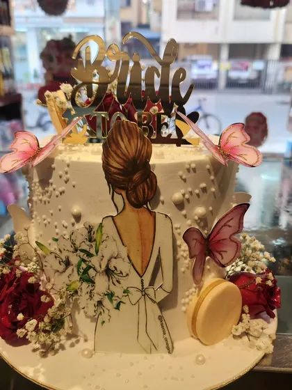 An elegant "Bride to be" cake designed for a bridal shower or bachelorette party. It features a beautiful illustration of a bride, delicate wafer paper butterflies, fresh flowers, and a golden topper, combining modern illustration with classic cake artistry.
