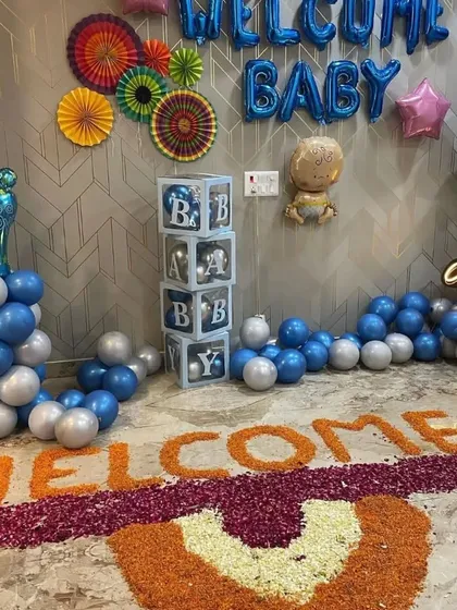 A complete "Welcome Baby" decoration for a baby boy, including blue and silver balloons, "BABY" display boxes, foil balloons, and a traditional flower petal "WELCOME" message on the floor.
