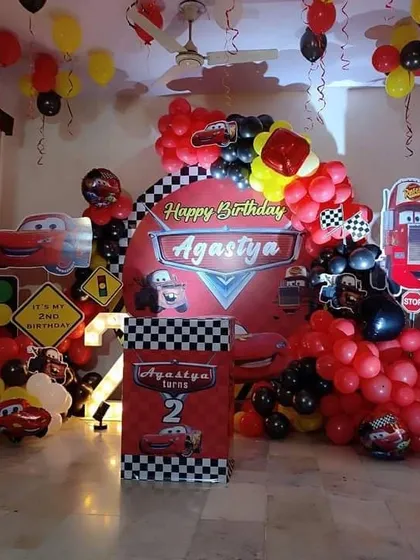 A high-energy Disney Cars theme for a 2nd birthday. This decoration features a checkered flag backdrop, Lightning McQueen cutouts, a marquee number '2', and a red and black balloon arch to create a racetrack feel right at home.