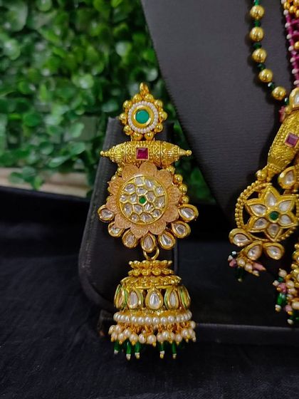 A close-up of a beautiful jhumka from a for-sale set. This earring showcases delicate floral kundan work and is finished with pearls and green beads.