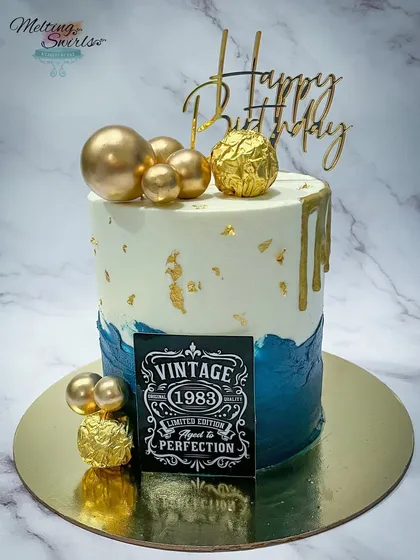 A 40th birthday milestone cake with a vintage "Aged to Perfection" theme. This buttercream cake combines a deep blue with white and gold for a masculine and stylish look.