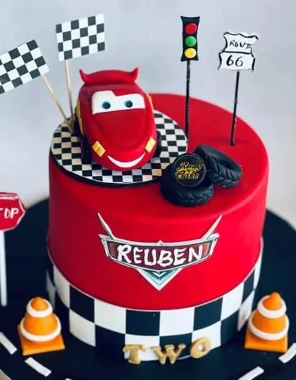 A "Cars" movie themed cake for a little fan named Reuben. This cake features Lightning McQueen on a racetrack, complete with traffic lights, cones, and checkered flags for a fun birthday.