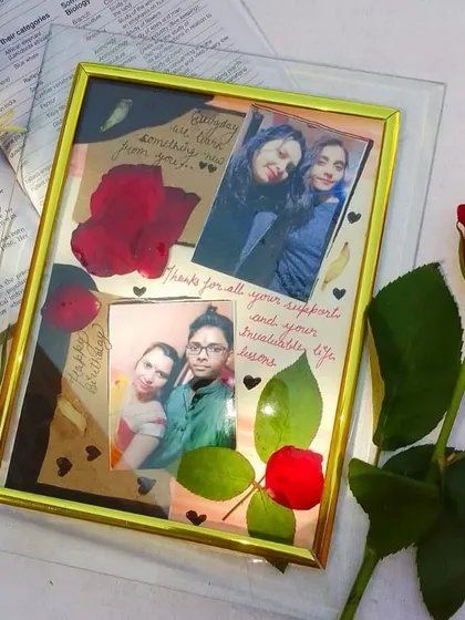 This custom frame combines photos with preserved natural elements like a real rose and leaves. It's a handmade piece that mixes pictures with handwritten notes for a scrapbook feel.