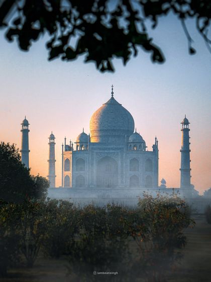 The Taj Mahal seen through a frame of morning mist and trees. This photo captures a soft, ethereal mood, different from the usual bright and sunny shots of the monument.
