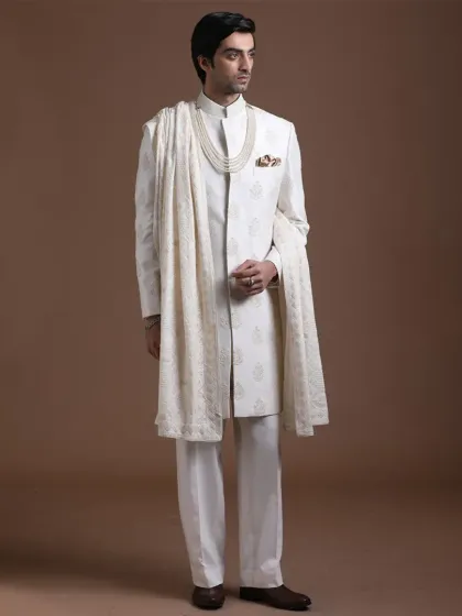A full-length view of an all-white sherwani ensemble, accessorized with a traditional pearl necklace and an embroidered shawl. This look is the epitome of royal elegance, designed for a groom who wants to make a classic and powerful statement.