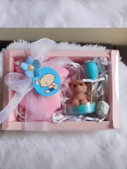 A cute baby shower return favor box, containing a baby romper soap and a teddy bear candle.