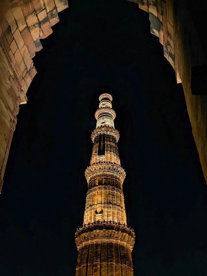 The iconic Qutub Minar at night, viewed through an ancient archway, emphasizing its towering height and historical significance.