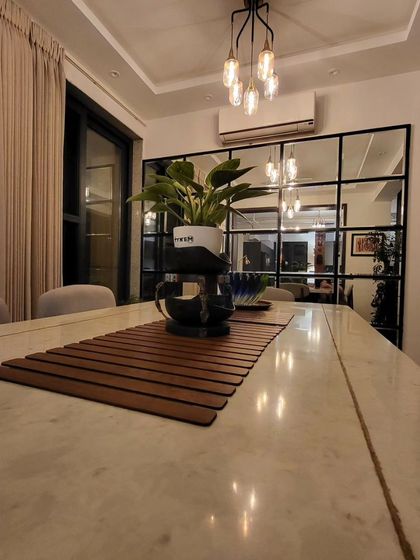 A full mirror wall with a modern black grid pattern visually doubles the size of this dining area, adding depth and reflecting light throughout the space.