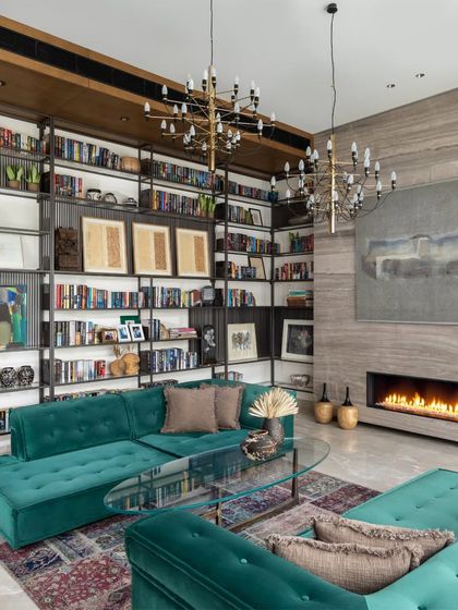 The library in the K Residence is a book lover's dream. Floor-to-ceiling metal and wood bookshelves are filled with the client's collection, while a plush velvet sectional in a striking teal offers a comfortable spot to read by the modern, stone-clad fireplace.