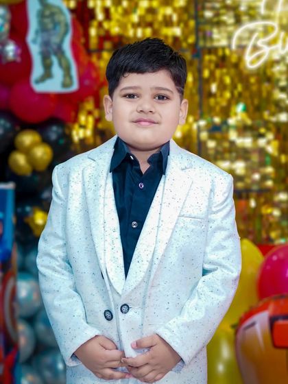 A young boy looks dapper and ready to celebrate in his smart white party suit.