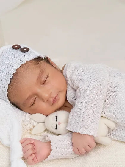 A two-week-old newborn snuggled with a tiny bunny toy, dressed in a cozy white knit outfit. This setup creates a feeling of warmth, innocence, and peaceful slumber.
