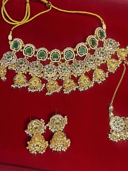 A flat-lay image of the green choker, earrings, and maang tikka, showing all the pieces you get when you rent this popular set.