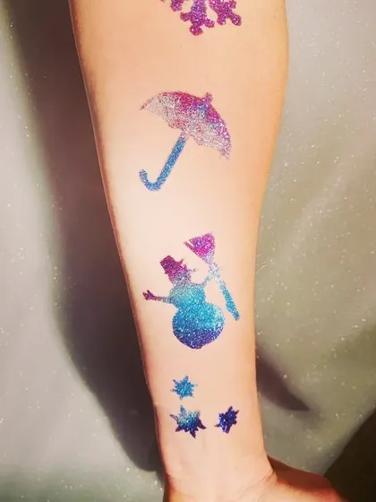 A collection of winter-themed glitter tattoos on an arm. This set includes a snowflake, an umbrella, a snowman, and little stars, perfect for a winter wonderland party.
