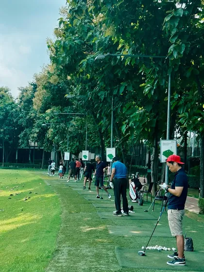 A player takes a moment to prepare, surrounded by the lush greenery and fellow golfers on a busy afternoon.